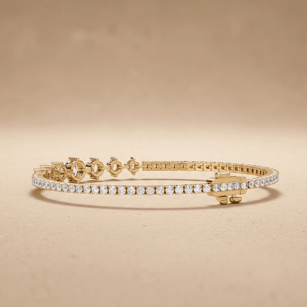 A gold tennis bracelet with a row of clear pavé-set stones and decorative gold clasp details, displayed on a warm beige background.