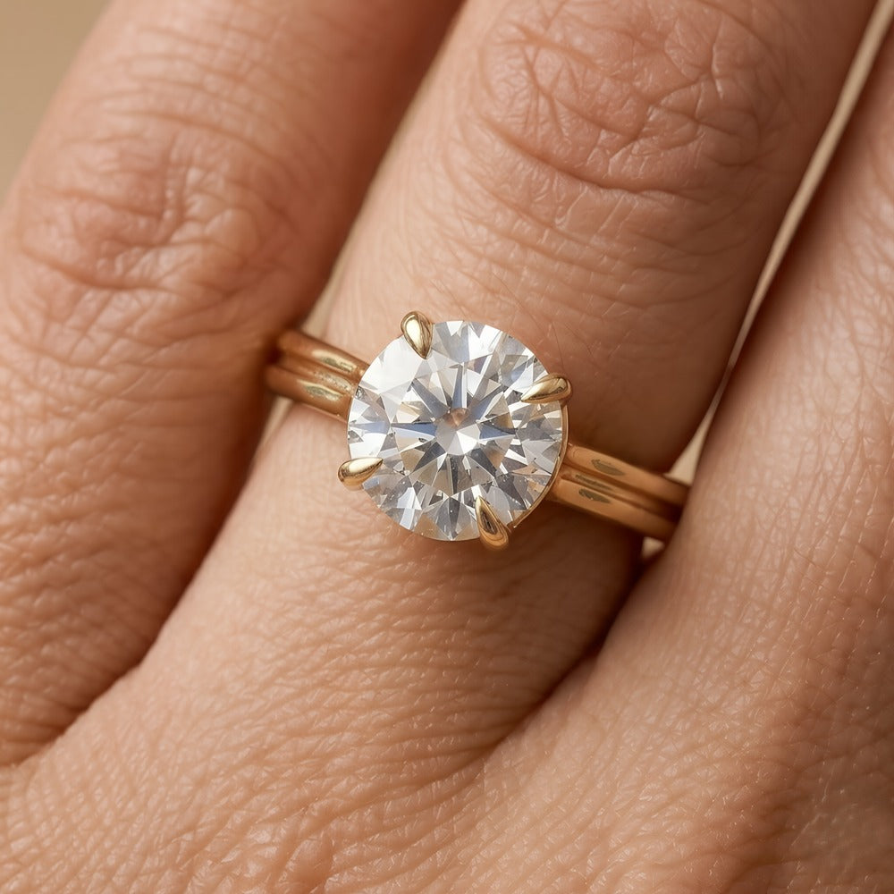 A close-up of a gold solitaire engagement ring with a round brilliant-cut diamond on a person's finger.