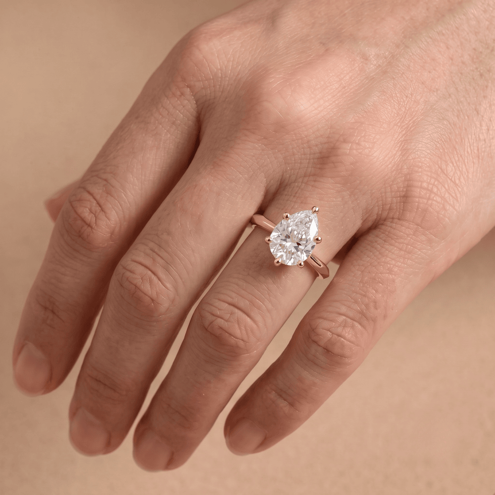 Pear shaped solitaire diamond ring worn on hand, 14K gold band