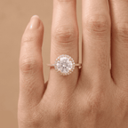 A close-up of a hand wearing a rose gold halo engagement ring with a round-cut center stone and small accent stones.