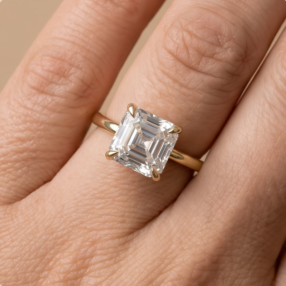 A close-up of a gold ring with an emerald-cut clear gemstone worn on a finger.