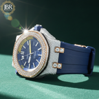 Luxury watch with blue strap and diamond-studded face on a green surface, branded 'JBR'.