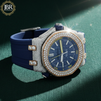 Luxury watch with blue strap and diamond-studded case on a green textured surface, featuring JBR Jewellers 