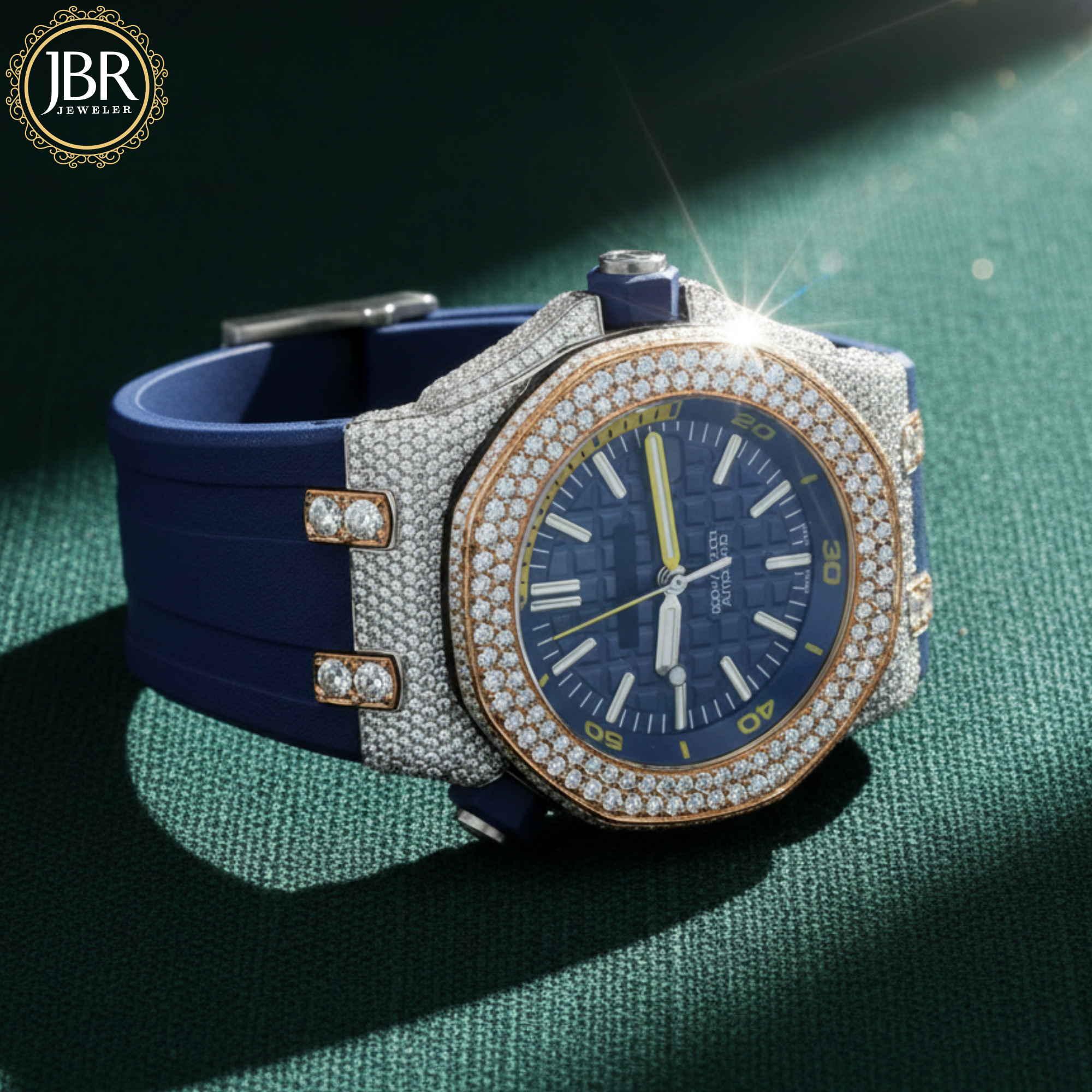 Luxury watch with blue strap and diamond-studded case on a green textured surface, featuring JBR Jewellers 