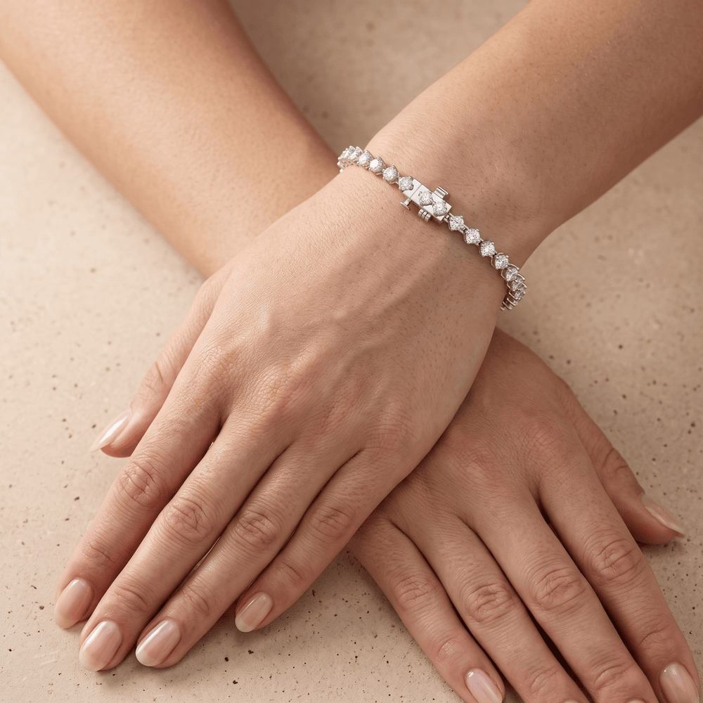 A close-up of a woman's hands and wrist wearing a delicate silver tennis bracelet with clear gemstones, resting on a textured beige surface.