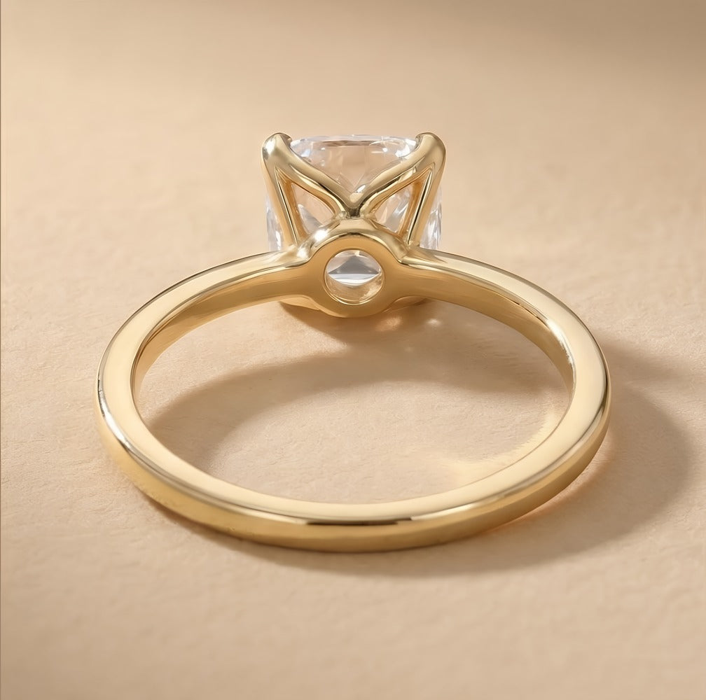 A gold ring with a clear rectangular gemstone in a four-prong setting, photographed on a warm beige background.