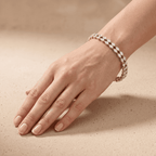 A close-up of a person's hand and wrist wearing a delicate rose gold bracelet with small clear stones, set against a warm beige textured background.