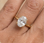 A yellow gold ring with a large oval-cut clear gemstone in a four-prong setting, shown worn on a finger.