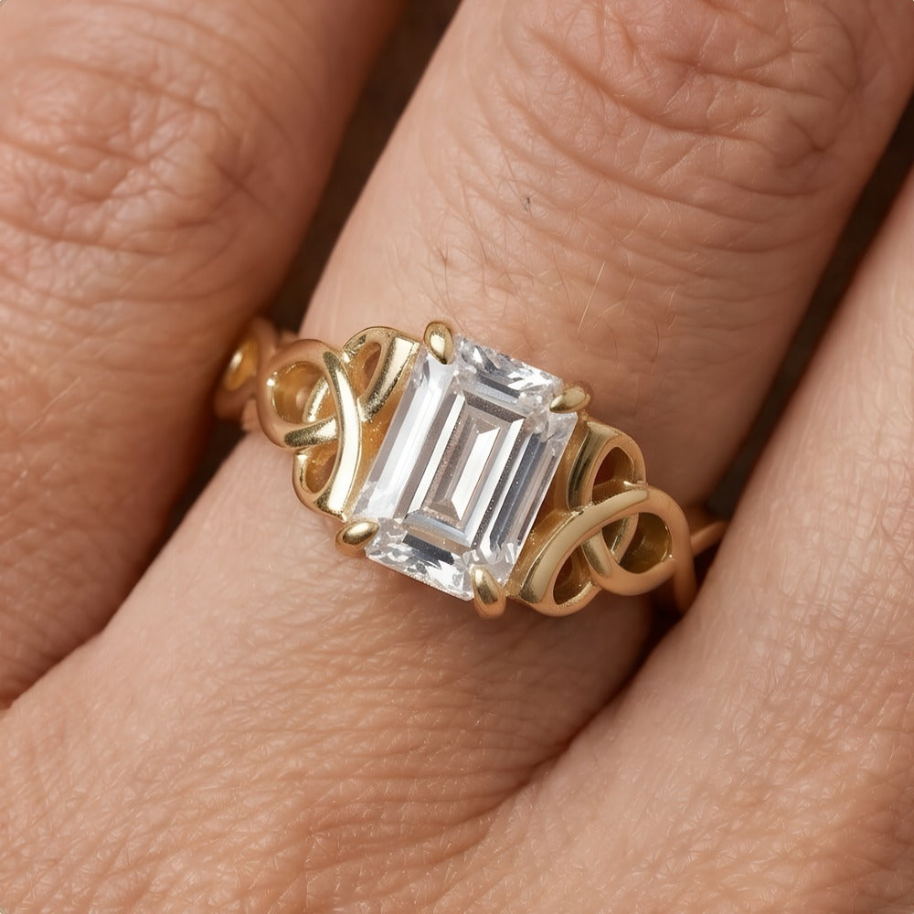 A gold ring with an emerald-cut clear center stone and decorative side stones, shown worn on a finger.