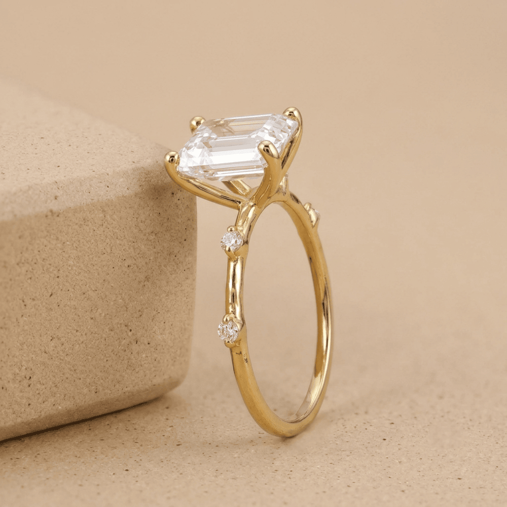 Slim gold engagement ring with emerald cut center stone