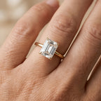 A close-up of a hand wearing a yellow gold ring with an emerald-cut clear gemstone.