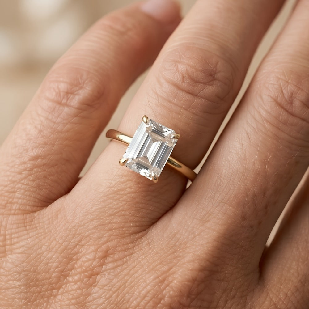 A close-up of a hand wearing a yellow gold ring with an emerald-cut clear gemstone.