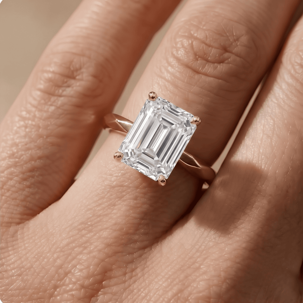 A close-up of a rose gold ring with a large emerald-cut clear gemstone, worn on a finger.
