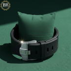 Black watch with silver clasp on a green cushion against a dark green background, featuring JBR Jewels 