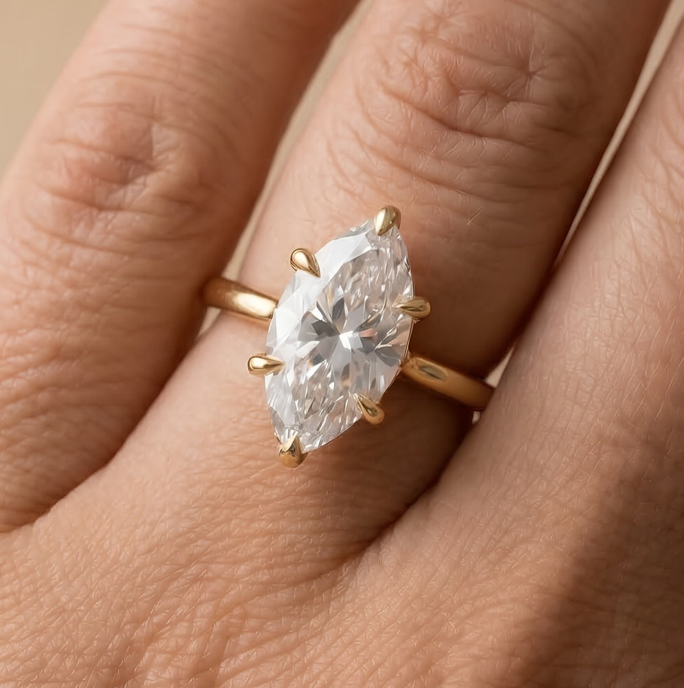 A close-up of a gold ring with a large marquise-cut clear gemstone worn on a finger.