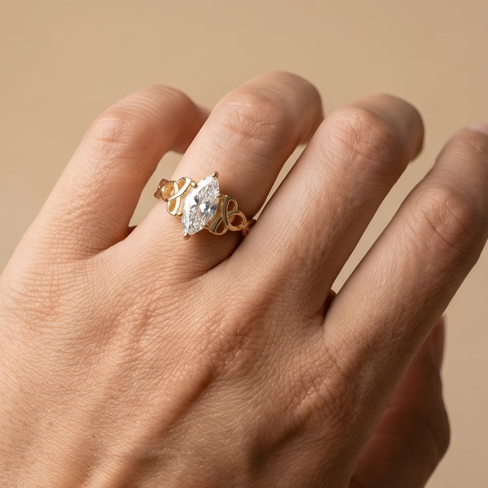 A gold ring with a marquise-cut clear gemstone worn on a person's finger, shown against a soft beige background.