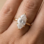 A close-up of a gold ring with a large marquise-cut clear gemstone worn on a finger.
