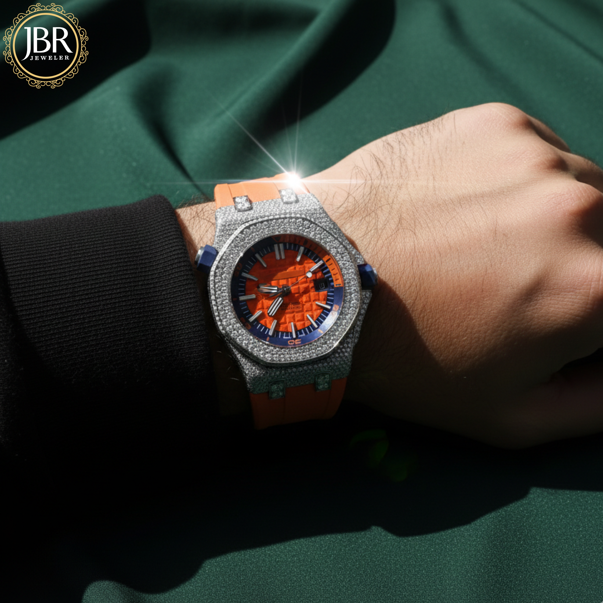 Luxury watch with orange and blue face on a wrist against a green fabric background, featuring JBR Jeweler