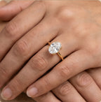 A close-up of a gold ring with a round clear gemstone worn on a person's finger, shown against skin tones.