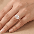 A close-up of a hand wearing a rose gold ring with a large oval-cut clear gemstone, set against a soft beige background.
