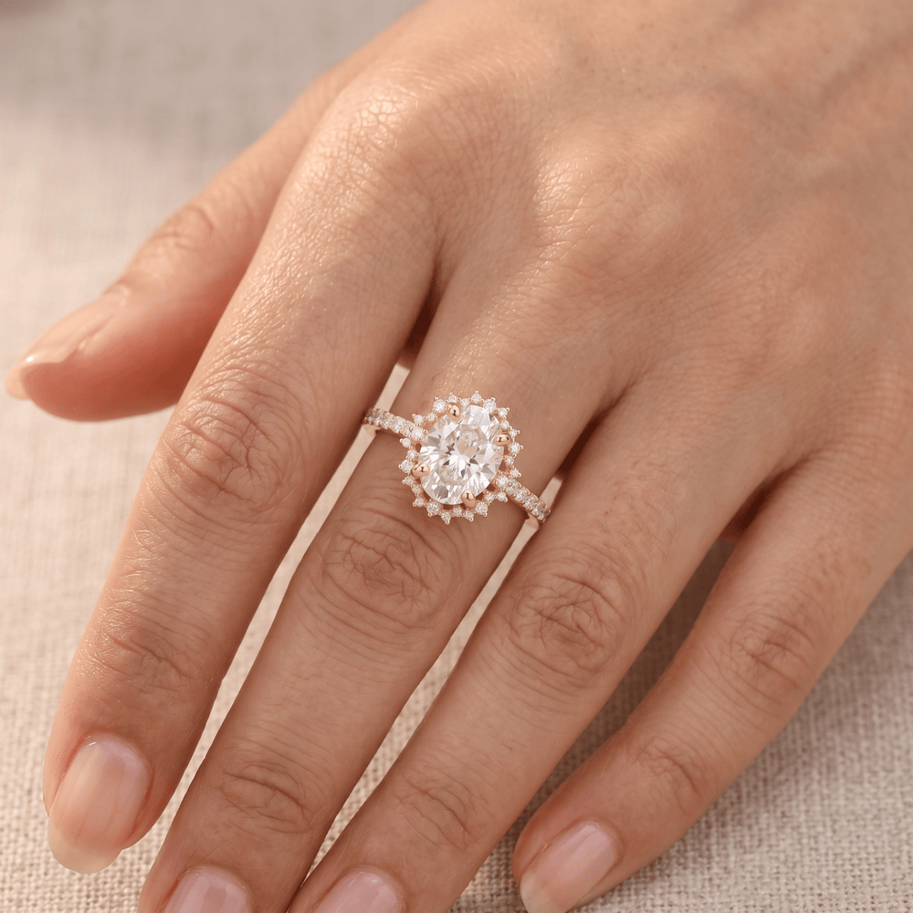 A close-up of a hand wearing a silver-toned ring with a large oval clear center stone and small clear accent stones around it, set against a soft neutral fabric background.