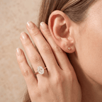 A close-up lifestyle shot of a woman's hand and ear, showcasing a rose gold ring with a marquise-cut clear gemstone on her ring finger, alongside a matching rose gold stud earring.