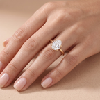 A close-up of a hand wearing a gold ring with a large clear heart-shaped gemstone in a prong setting, photographed against a soft beige background.
