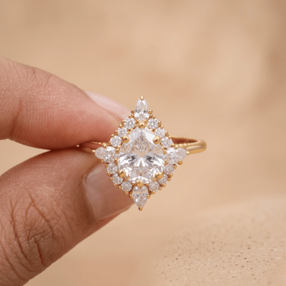 A close-up of a hand holding a gold ring with a large clear marquise-cut center stone and surrounding diamond-like accents, set against a soft beige background.