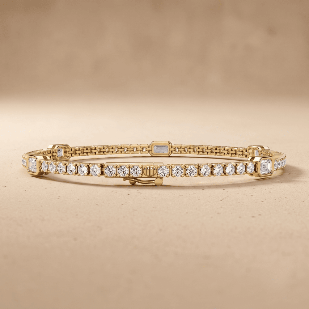 A gold tennis bracelet with clear round and rectangular gemstones, displayed on a textured beige background.