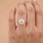 A close-up of a hand wearing a rose gold halo engagement ring with a large round center stone and small accent stones.