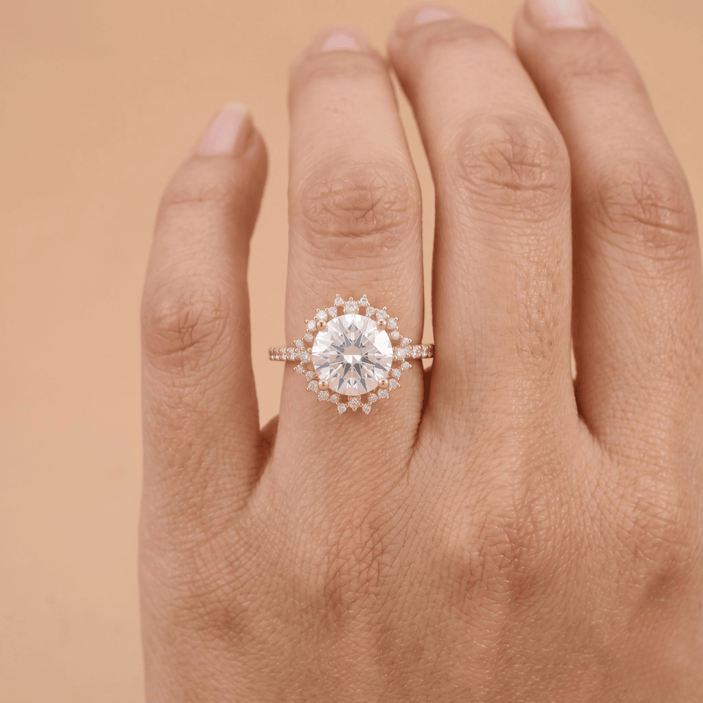 A close-up of a hand wearing a rose gold halo engagement ring with a large round center stone and small accent stones.