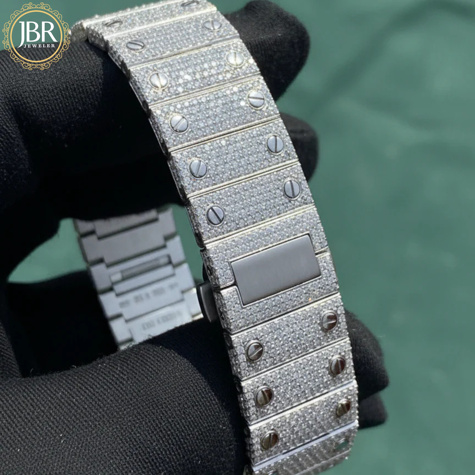 Silver watch band with diamond-like coating held by a gloved hand against a green background, JBR Jewellers logo visible.