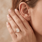 A close-up lifestyle shot of a woman wearing a rose gold engagement ring with a round brilliant-cut diamond on her ring finger, with a small matching rose gold stud earring on her ear.